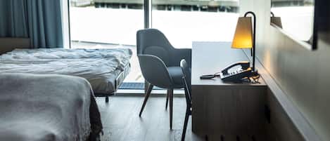 A hotel room with a bed, a desk with a lamp, and a chair.