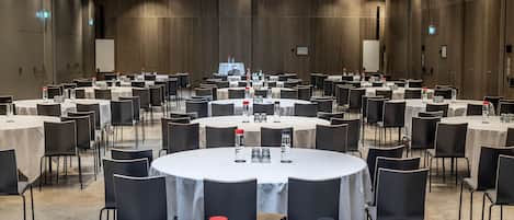 A large conference room with multiple round tables, each set with chairs and equipped with water bottles, glasses, and nameplates.