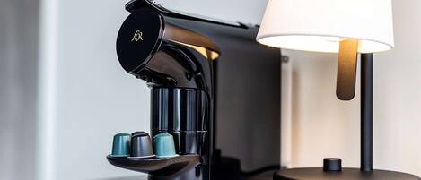 A modern coffee machine with a sleek design, a lamp, and a coiled cable on a wooden surface.