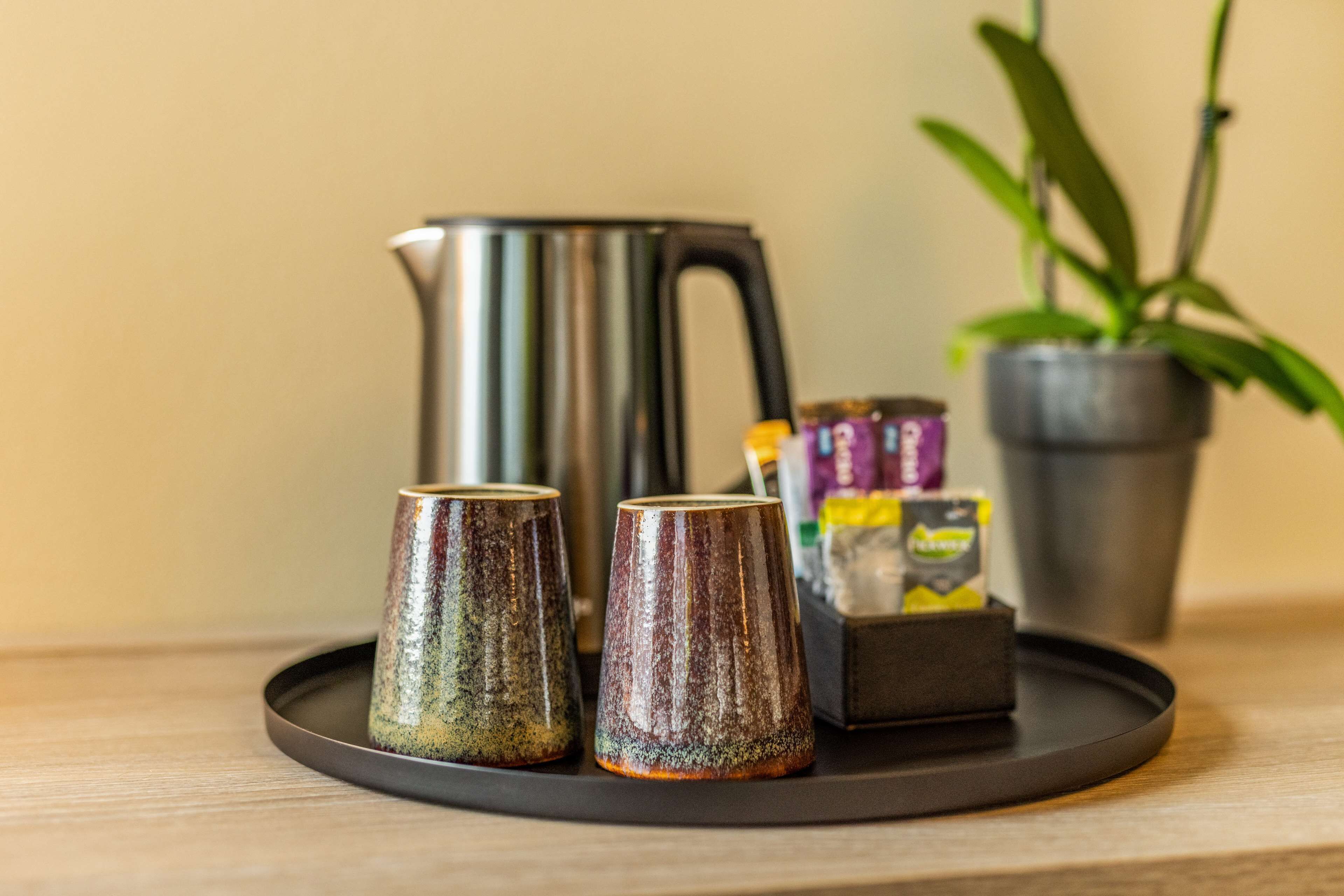 A tray with two ceramic cups, a coffee pot, and a box of tea bags on a wooden surface.