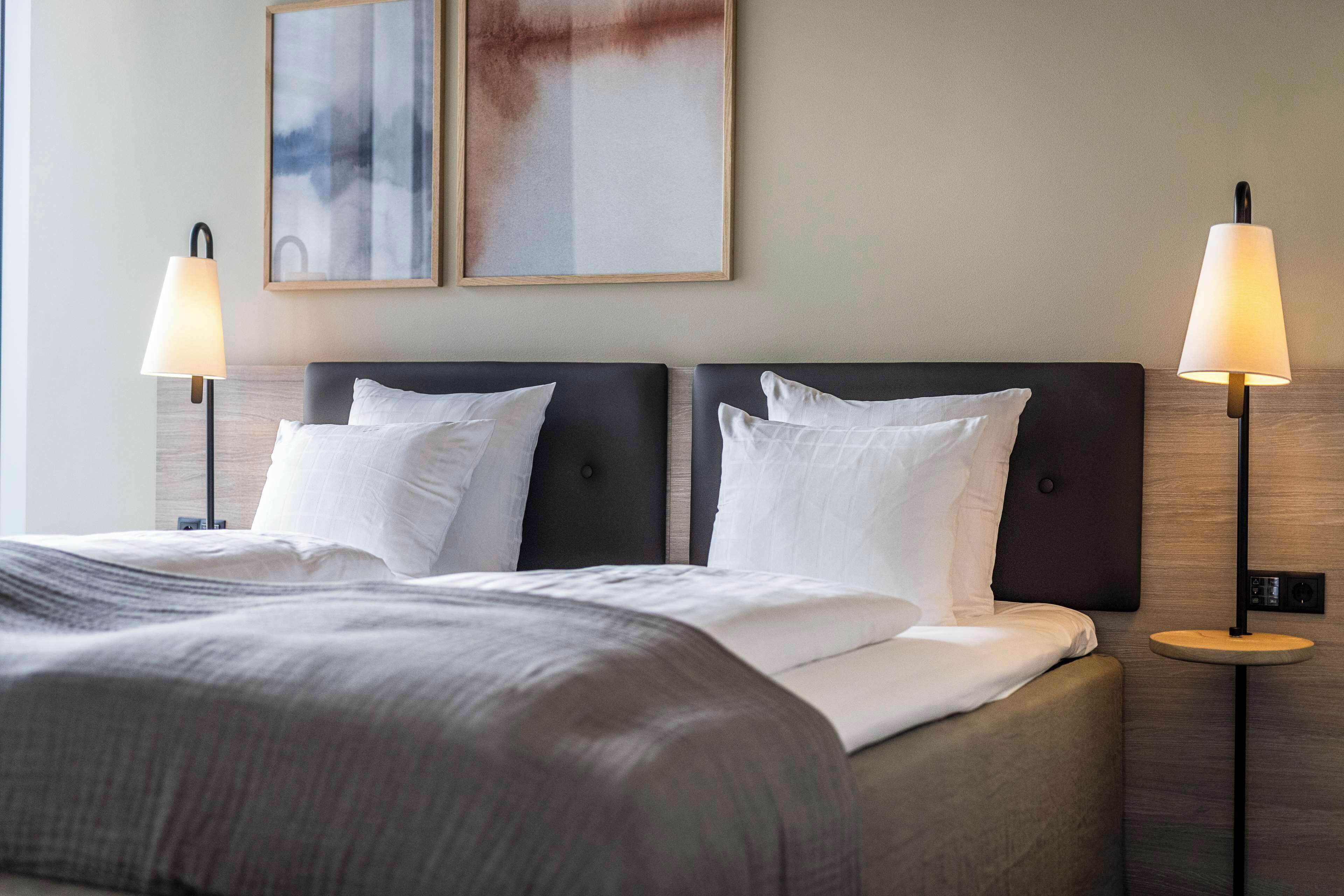 Una habitación de hotel con una cama grande, dos lámparas de noche y dos cuadros abstractos en la pared.
