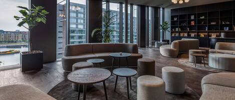 A modern lounge area with sofas, round tables, and a bookshelf.