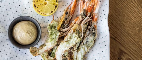 Une assiette de crevettes cuites, arrosées de jus de citron, et un bol de sauce.