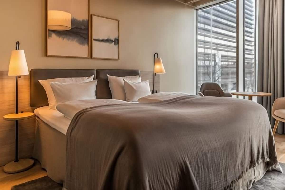 Une chambre d’hôtel moderne avec un grand lit, deux lampes de chevet, une petite table et une chaise.