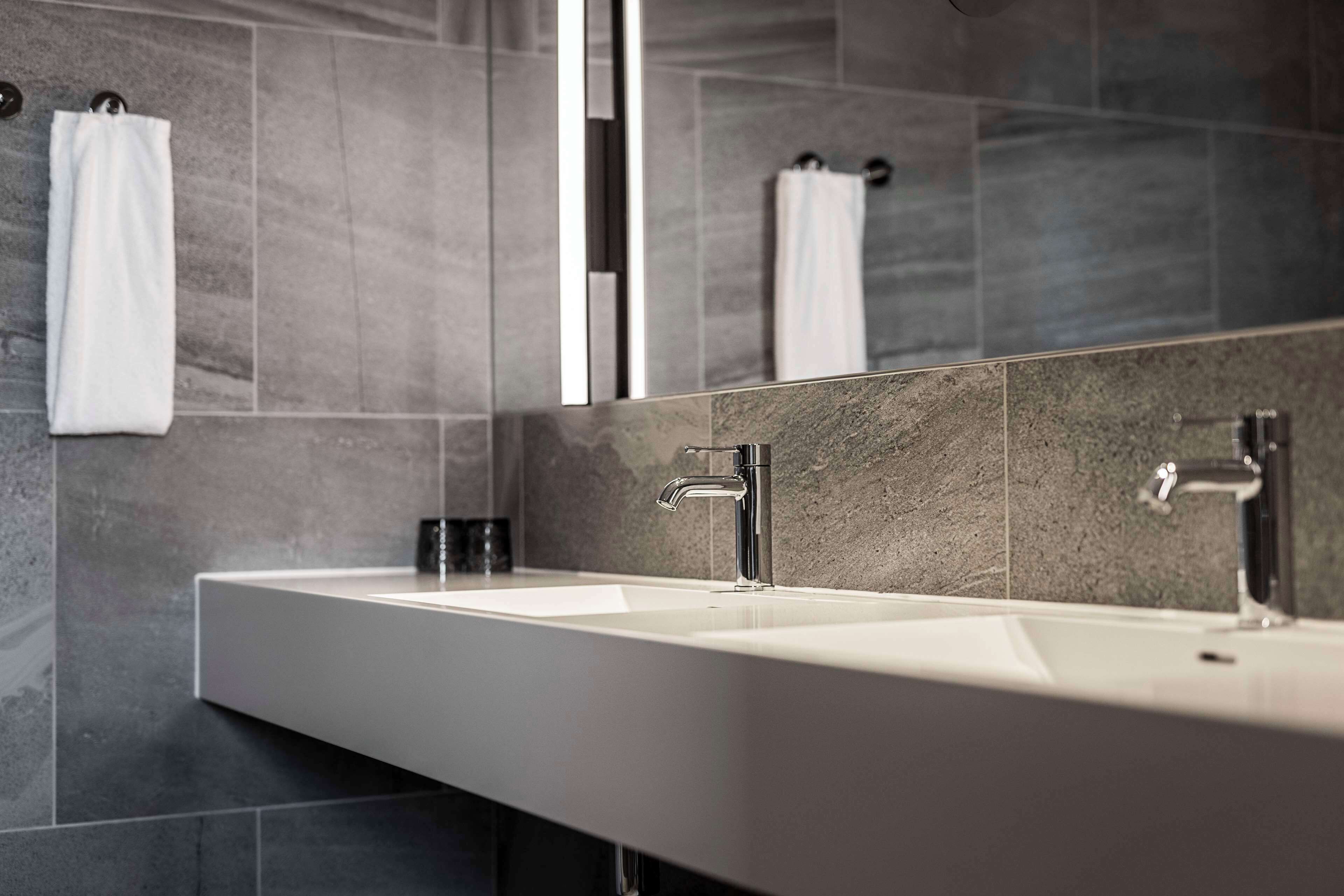 A modern bathroom with a white sink, two faucets, and a large mirror.