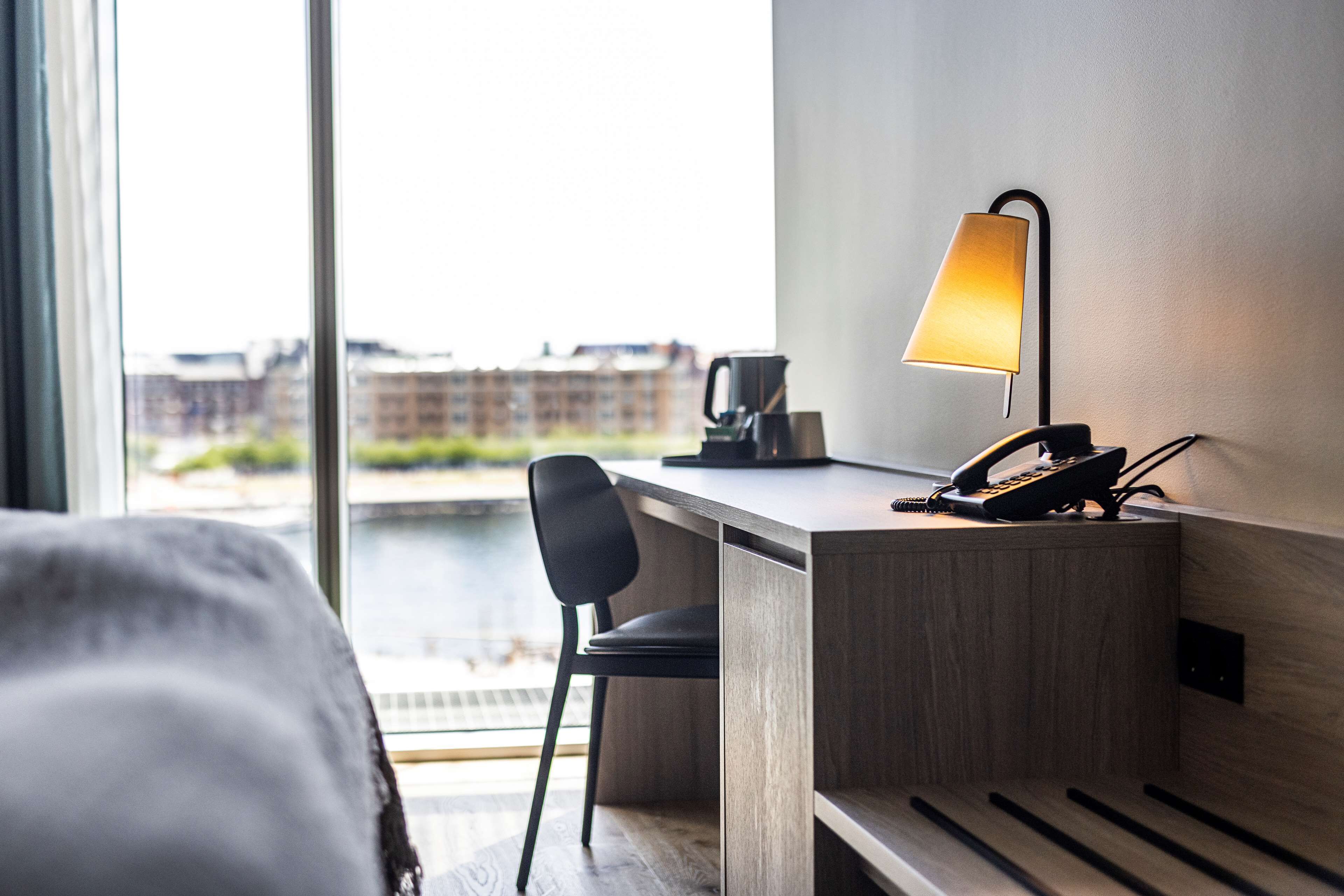 Una habitación de hotel con una cama, un escritorio con lámpara, una silla y un teléfono.