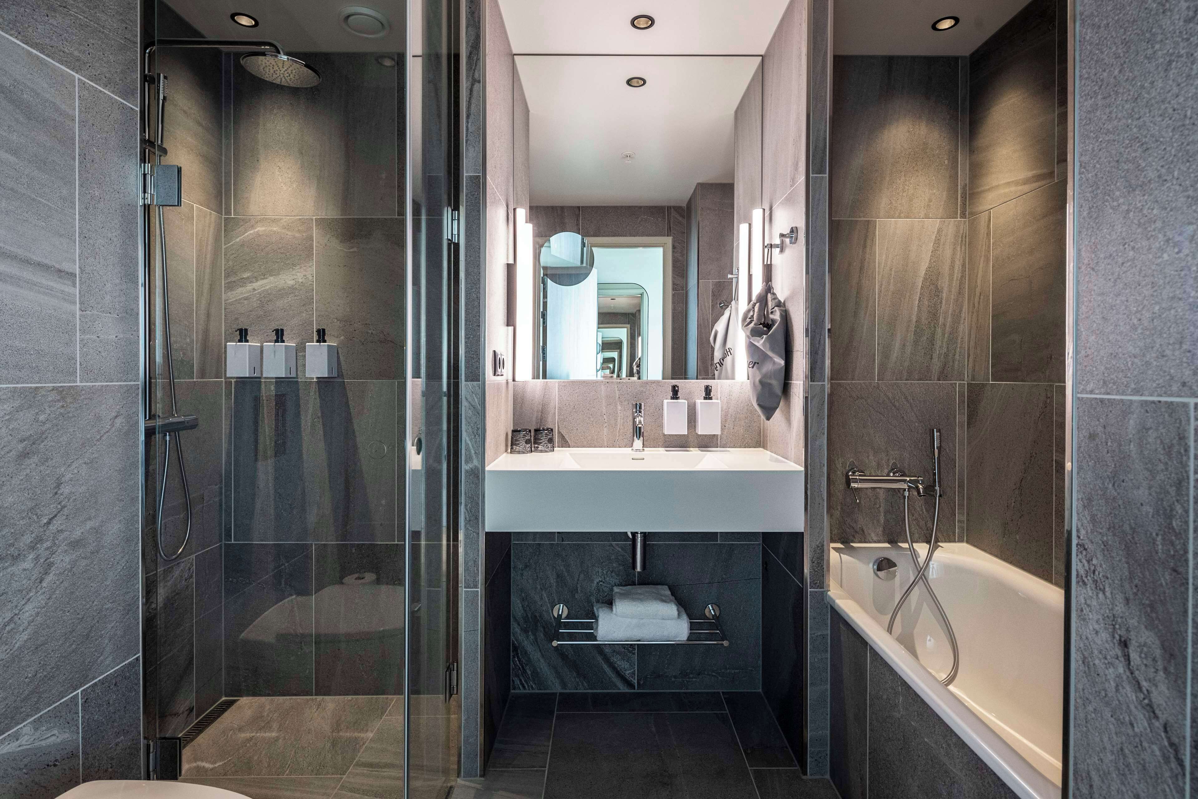Un baño moderno con ducha envuelta en vidrio, un lavabo central y una bañera.