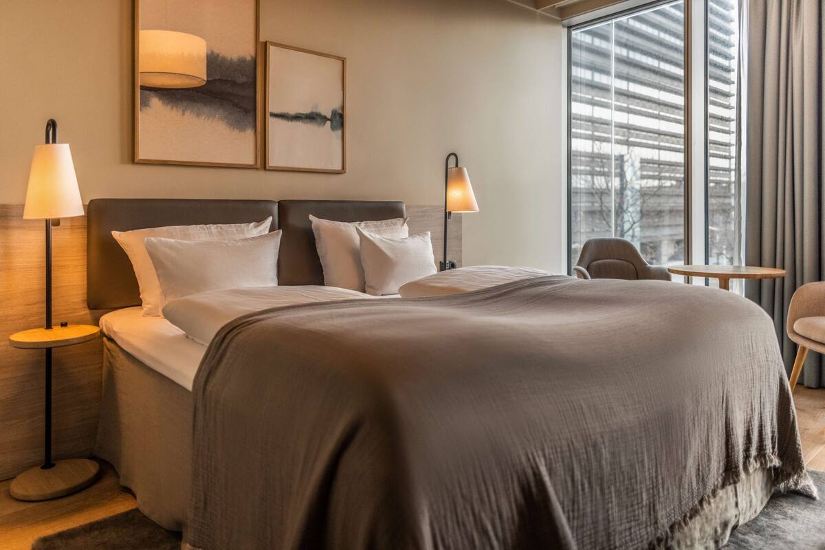 Une chambre d’hôtel moderne avec un grand lit, deux lampes de chevet, une petite table et une chaise.
