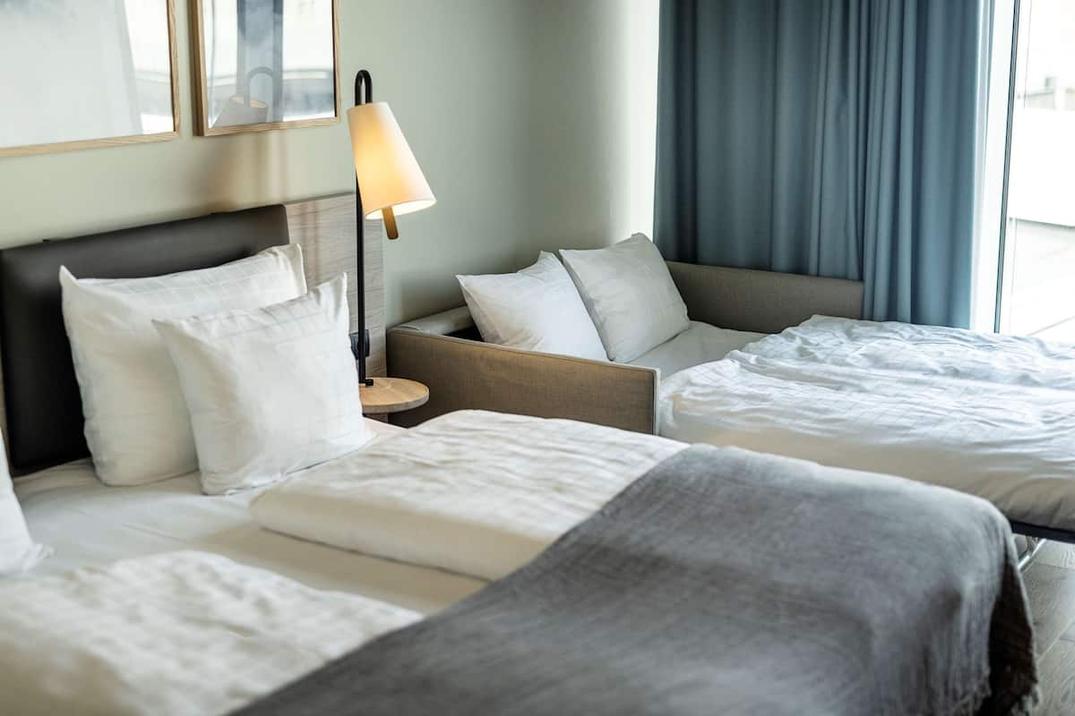 Une chambre d’hôtel avec deux lits, une table de chevet avec une lampe et une fenêtre avec des rideaux.