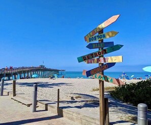 A beach with a wooden signpost with city names pointing in different directions.