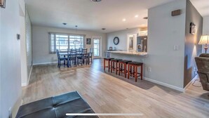 A spacious living area with a dining table and chairs, a kitchen with a bar, and a large window providing natural light. - 🏝️PET FRIENDLY 3-bedroom house, minutes from Beach,Heated Pool (Venice)