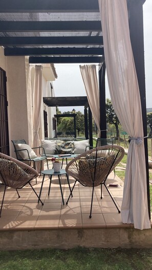An outdoor patio with wicker furniture, a glass table, and a pergola with white curtains.