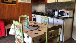 Et køkken med træskabe, en mikrobølgeovn, en kaffemaskine og et bord med et mønstret duge.