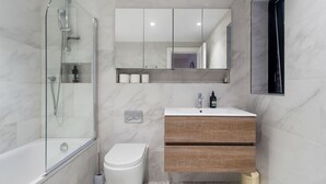 A modern bathroom with a glass-enclosed shower, a white toilet, a wooden vanity with a mirror, and a white sink. - Cosy one bedroom apartment in Highgate, close to Hampstead heath (London)