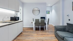 A modern kitchen with white cabinets, a built-in microwave, and a dining area with a table and chairs. - Cosy one bedroom apartment in Highgate, close to Hampstead heath (London)