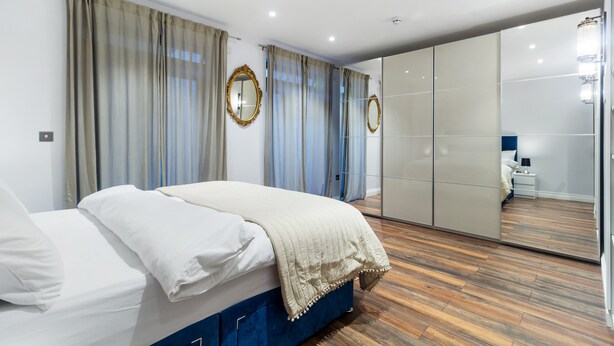 A modern bedroom with a bed, curtains, a mirror, and a wardrobe. - Cosy one bedroom apartment in Highgate, close to Hampstead heath (London)