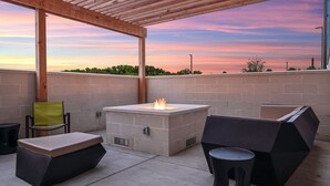 An outdoor patio with a fire pit, seating, and a view of the sunset.