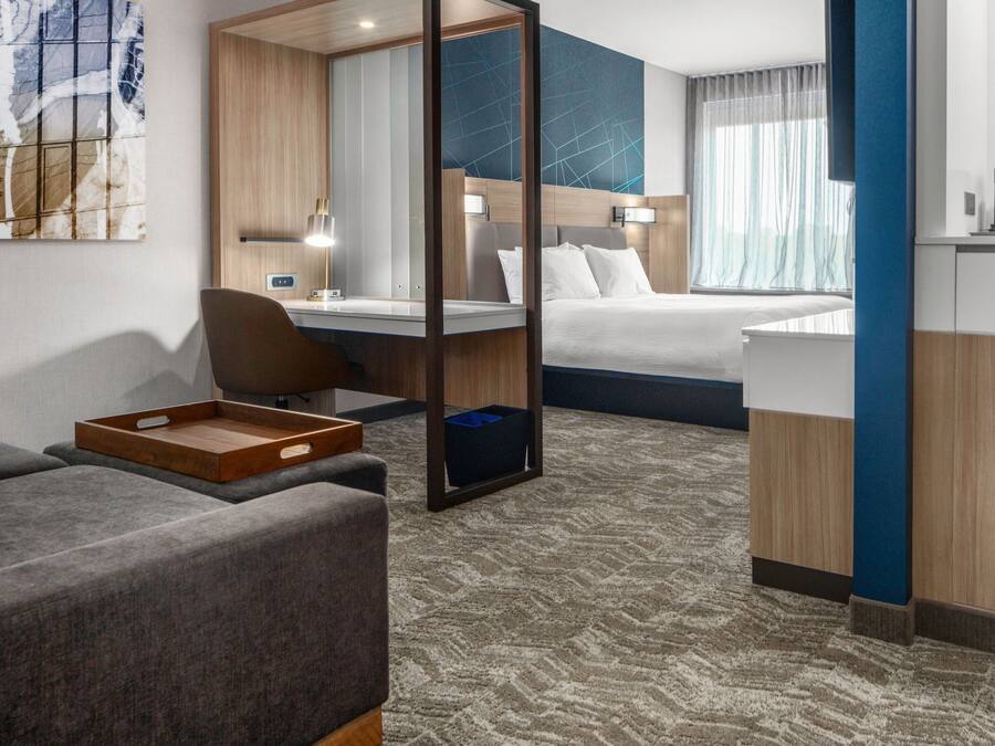 A hotel room with a bed, a desk, a chair, a sofa, a tray, and a large mirror.
