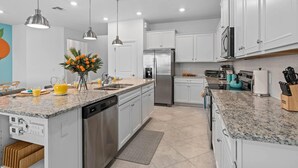 A modern kitchen with white cabinets, granite countertops, stainless steel appliances, and pendant lighting. - 8BR Retreat | Sleep 20 | Theater | Huge Pool & Spa (Davenport)