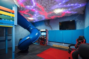 Un espace de jeux avec un toboggan, des jeux d’arcade et un téléviseur fixé au mur.