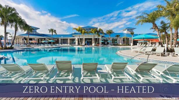 A zero entry pool with a heated water feature, surrounded by lounge chairs and umbrellas, with a building in the background. - 8BR Retreat | Sleep 20 | Theater | Huge Pool & Spa (Davenport)