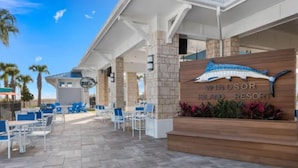 An outdoor seating area with blue chairs and tables, a wooden sign with a shark design, and palm trees in the background. - 8BR Retreat | Sleep 20 | Theater | Huge Pool & Spa (Davenport)