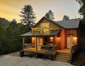 A wooden cabin with a balcony, a porch, and a staircase leading to the entrance.