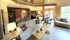 Un salon spacieux avec un plafond haut, des poutres apparentes, un grand canapé, une table basse et un coin repas avec des bancs.