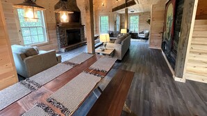 L’intérieur d’un chalet confortable, avec une cheminée en pierre, des poutres en bois et une longue table à manger agrémentée de sets de table.