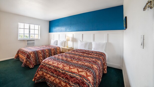 Une chambre d’hôtel avec deux lits, une fenêtre, une tête de lit blanche et un mur d’accent bleu.