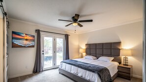 Een slaapkamer met een bed, twee nachtkastjes met lampen, een plafondventilator en een groot raam met gordijnen.
