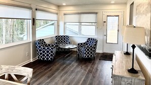 A room with a wooden floor, two patterned chairs, a small table, a lamp, and large windows with blinds. - Centrally Located Cozy House,2 king beds,Game Room (Greensboro)