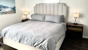 A bedroom with a large bed, two bedside tables with lamps, a ceiling fan, a painting on the wall, and a window with blinds. - Centrally Located Cozy House,2 king beds,Game Room (Greensboro)
