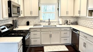 A modern kitchen with white cabinets, a stove, microwave, and a window providing natural light. - Centrally Located Cozy House,2 king beds,Game Room (Greensboro)