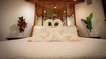 A neatly made bed with a large mirror above it, a potted plant to the right, and a wooden ceiling structure.