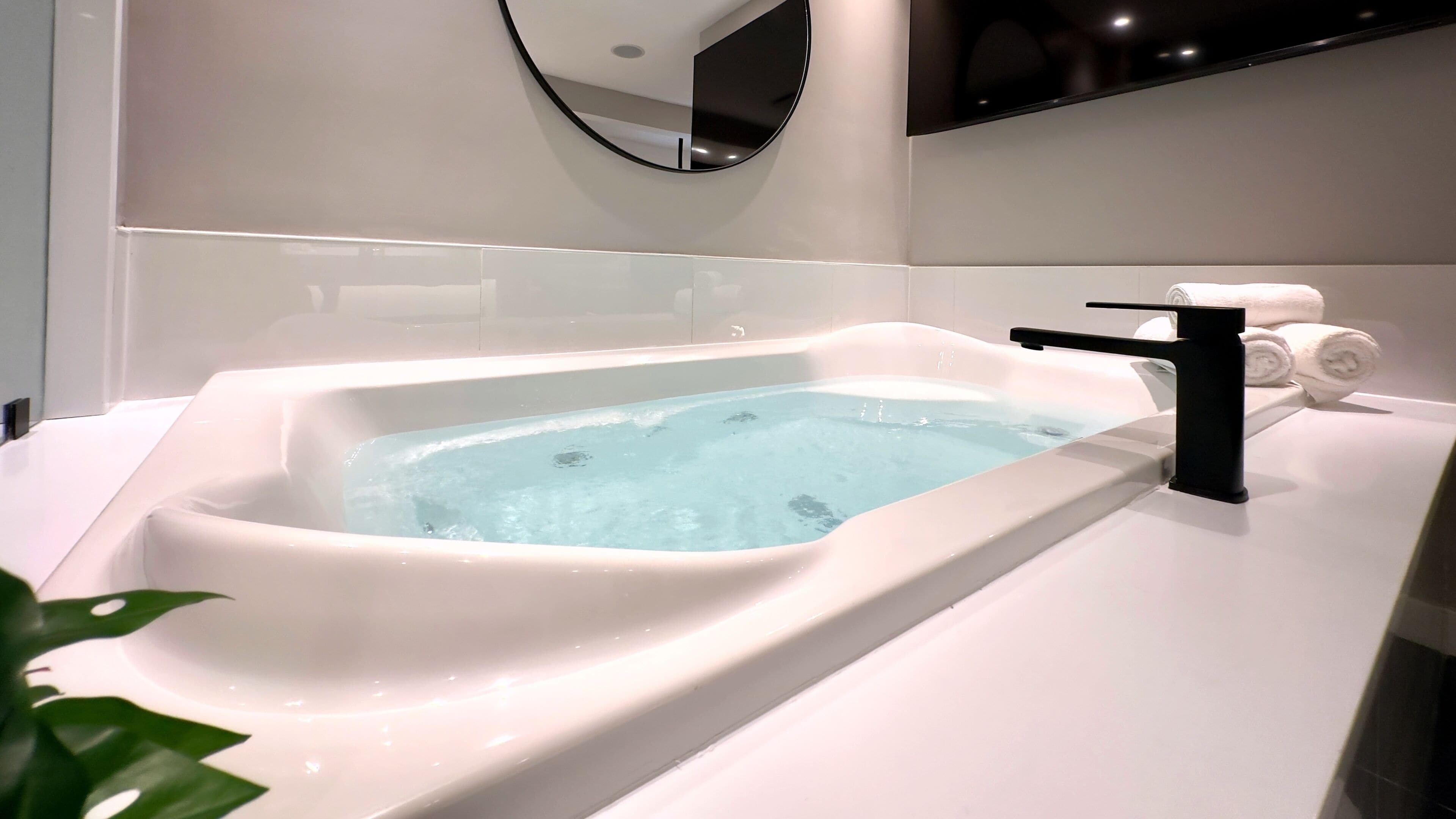 Un bagno moderno con una vasca da bagno rettangolare, un rubinetto nero e un portasciugamani con asciugamani.