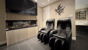 Ein moderner Spa-Raum mit Massageliegen-Bereich, einem an der Wand befestigten Fernseher und einem dekorativen Wandbild.