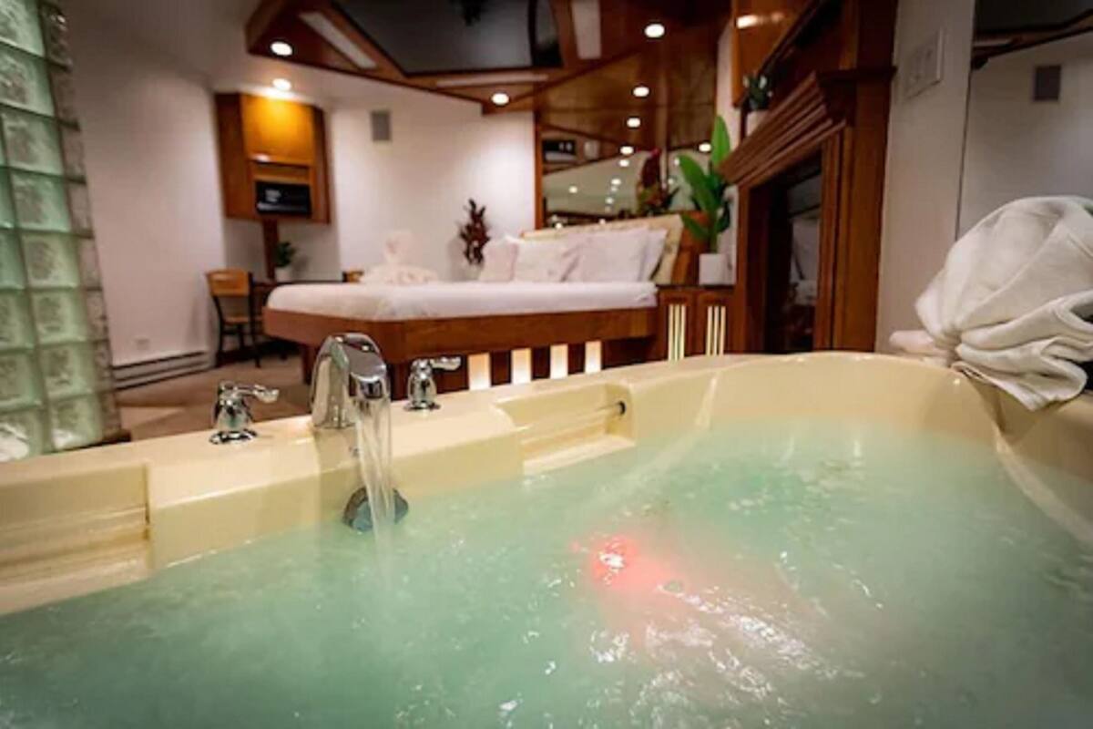 A room with a large bathtub, a bed, a desk, and a mirror.
