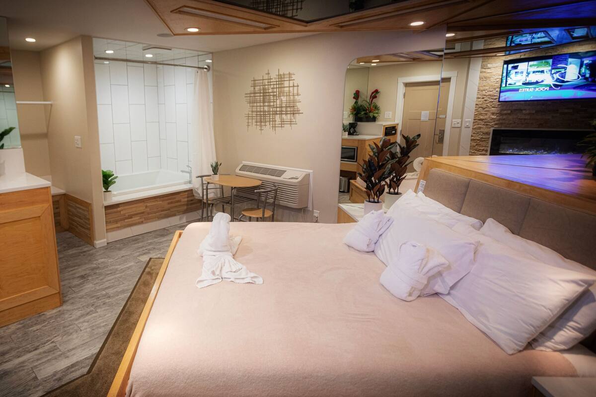 A hotel room with a bed, a desk, a chair, a small table, and a TV.