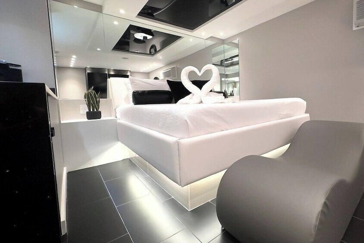 A modern bedroom with a bed, a chair, and a unique heart-shaped mirror.
