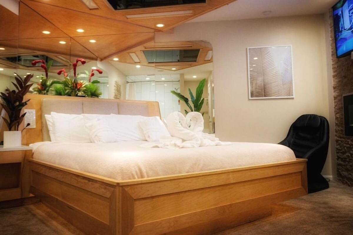 A hotel room with a wooden bed, a TV on the wall, and a plant on the bedside table.