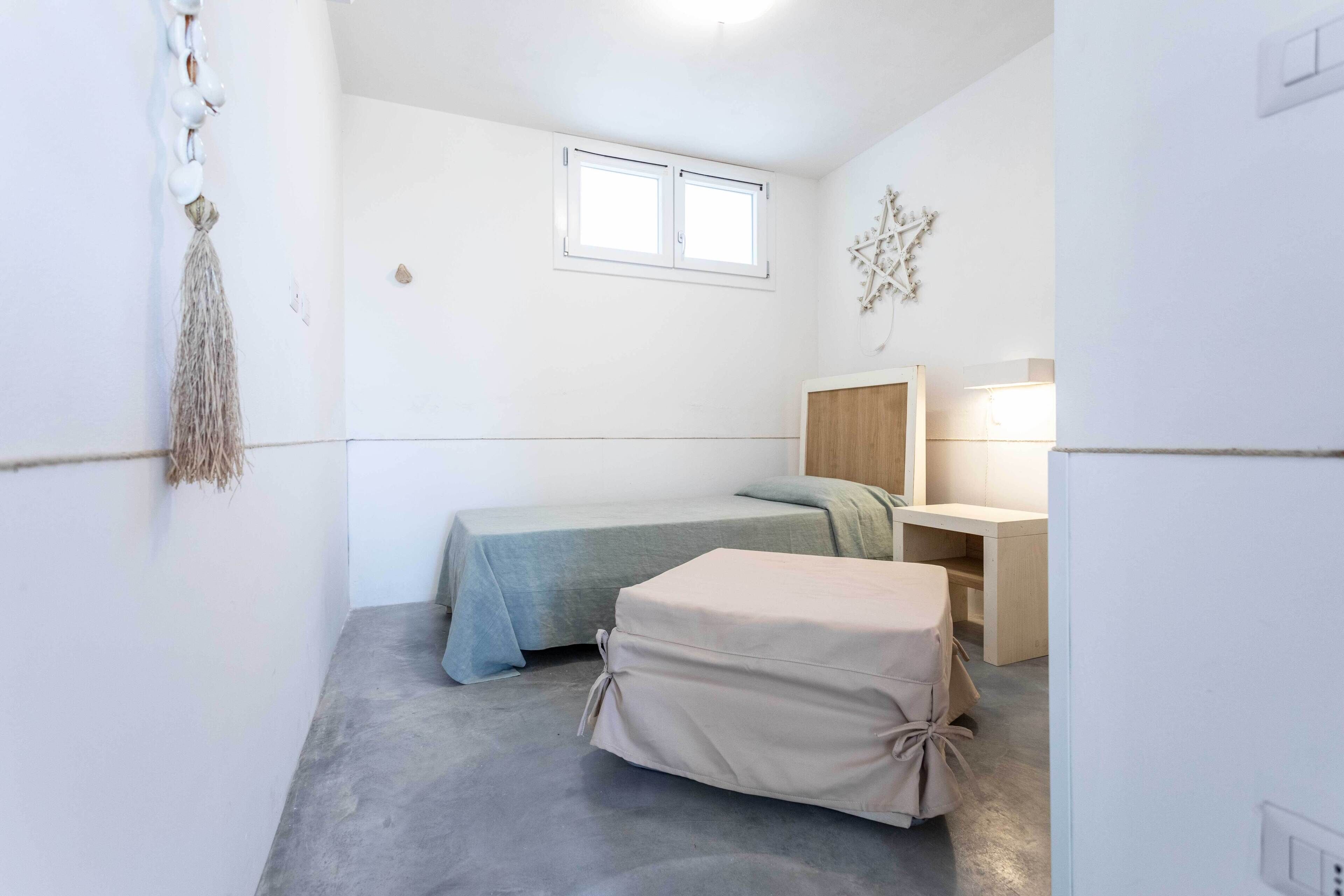 A small, compact bedroom with a single bed, a bedside table, a nightstand, and a window.