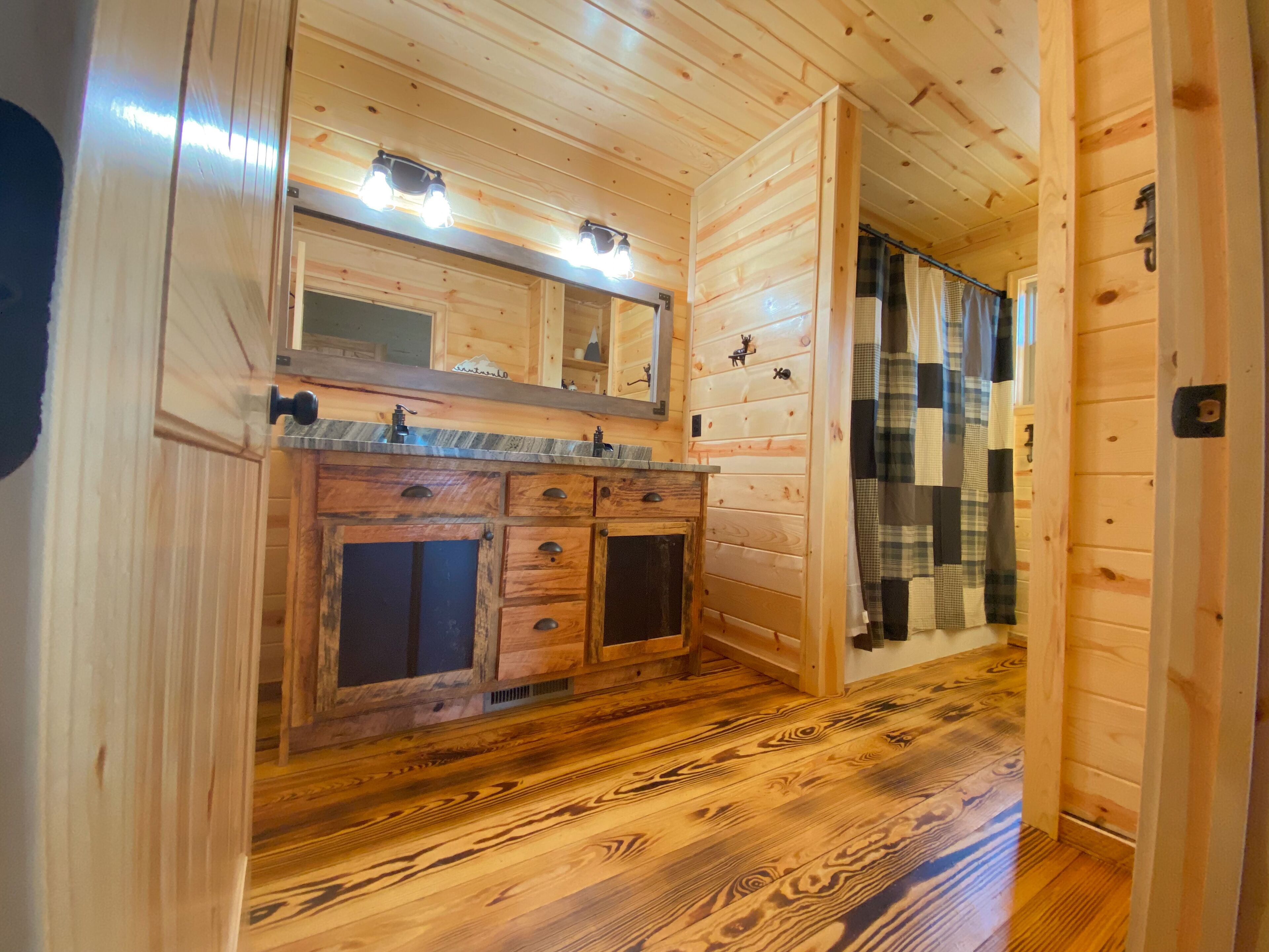 Een houten interieur met een houten vloer, een wastafel met spiegel erboven en een deur naar een andere kamer.