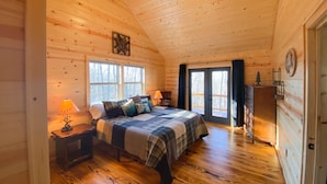 A cozy log cabin bedroom with a bed, nightstands, a ceiling fan, and a large window. - 🪵 Murphy Cabin 🏔 Mountain View // 2Bed-2Bath // 6 guests // 10mins to town (Murphy)