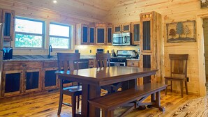 A wooden cabin interior with a kitchen, dining area, and large windows. - 🪵 Murphy Cabin 🏔 Mountain View // 2Bed-2Bath // 6 guests // 10mins to town (Murphy)