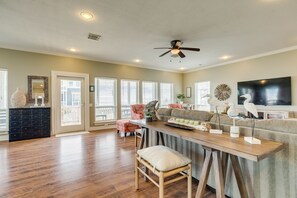 Un salon spacieux doté de planchers en bois franc, d’un ventilateur de plafond, d’un grand téléviseur à écran plat et d’un coin repas avec une table et des chaises en bois.
