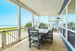 Eine überdachte Terrasse mit Tisch und Stühlen mit Blick auf Strand und Meer.