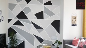 A modern living room with a geometric-patterned wall, a glass coffee table, a grey sofa with patterned cushions, and a yellow rug. - One Bedroom Apartment by Klass Living Serviced Accommodation Bellshill - Mossend  Apartment with WIFI  and Parking (Bellshill)