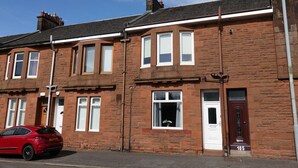 A red car parked in front of a brick building with a sign for 'Klass Living' indicating short lets and serviced accommodation. - One Bedroom Apartment by Klass Living Serviced Accommodation Bellshill - Mossend  Apartment with WIFI  and Parking (Bellshill)