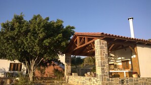 A stone building with a wooden pergola, outdoor seating, and a chimney.